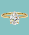 A pear-cut diamond engagement ring in a yellow gold band, centered against a solid light teal background.