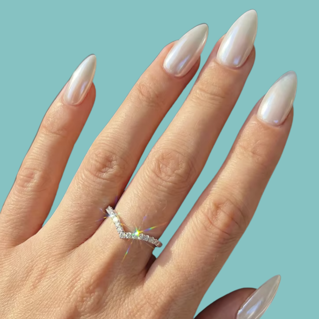 A close-up of a hand with long, glossy white manicured nails wearing a delicate silver V-shaped ring set with small sparkling stones, against a solid light teal background.