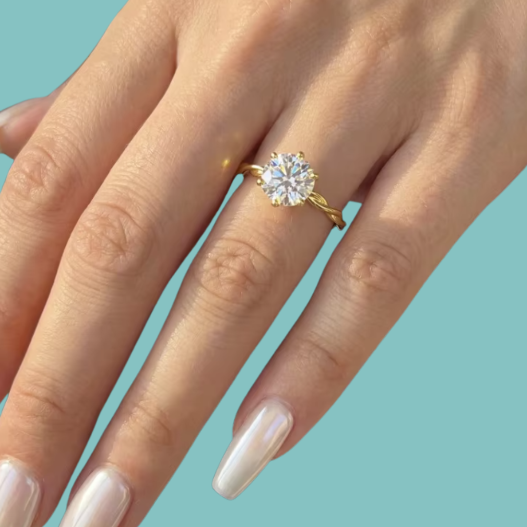 A close-up of a hand wearing a yellow gold ring with a round brilliant-cut diamond. The background is a solid light teal color.