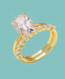 A yellow gold ring featuring a large oval-cut clear center stone and small clear accent stones along a split shank, shown on a solid light aqua background.