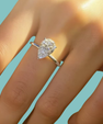 A pear-cut diamond ring on a silver band, shown worn on a person's finger against a solid light blue background.