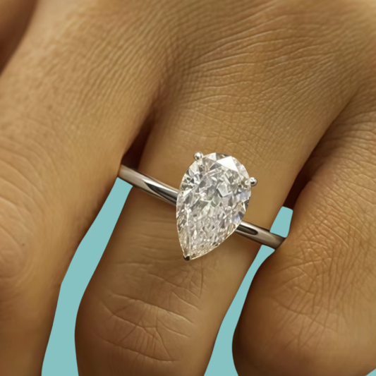 A pear-cut diamond ring on a silver band, shown worn on a person's finger against a light blue background.