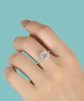 A silver-toned halo ring with a round-cut center stone and small accent stones, shown worn on a hand against a solid light blue background.