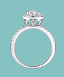 A silver-toned diamond ring with a round-cut center stone and a halo setting, shown against a solid light teal background.