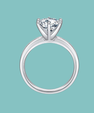 A silver solitaire engagement ring with a round brilliant-cut diamond, shown against a solid light teal background.