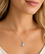 A close-up of a woman wearing a delicate silver chain necklace with a round clear gemstone pendant.