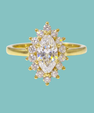A yellow gold ring featuring a marquise-cut clear center stone surrounded by a halo of small round clear stones, set against a solid light teal background.