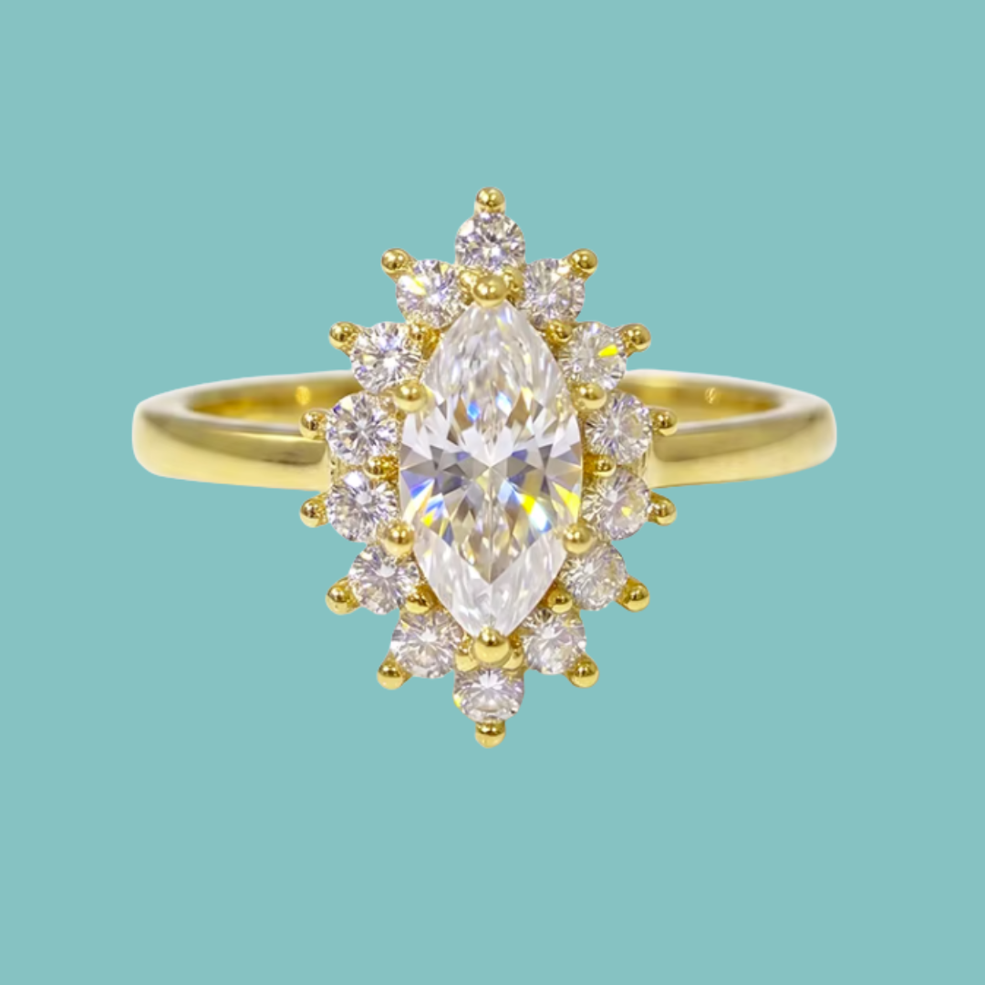 A yellow gold ring featuring a marquise-cut clear center stone surrounded by a halo of small round clear stones, set against a solid light teal background.