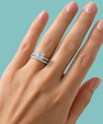 A close-up of a hand wearing a silver-toned double ring set with a large square-cut clear center stone and a matching pavé band, against a solid light aqua background.