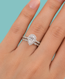 A close-up of a hand wearing a silver-toned ring set with a pear-cut diamond and smaller diamonds along the band, against a solid light blue background.