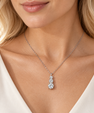 A close-up of a woman wearing a delicate silver chain necklace with a pear-shaped pendant set with clear gemstones, paired with a white top.