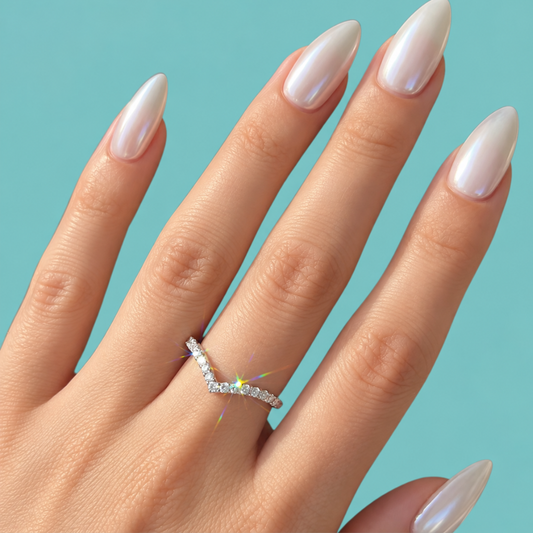 A close-up of a hand with long, glossy white manicured nails wearing a silver V-shaped ring set with small clear stones, against a solid light blue background.
