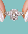 An oval-cut diamond engagement ring with a silver-toned band accented by small side diamonds, held between two fingers with iridescent nail polish against a solid teal background.