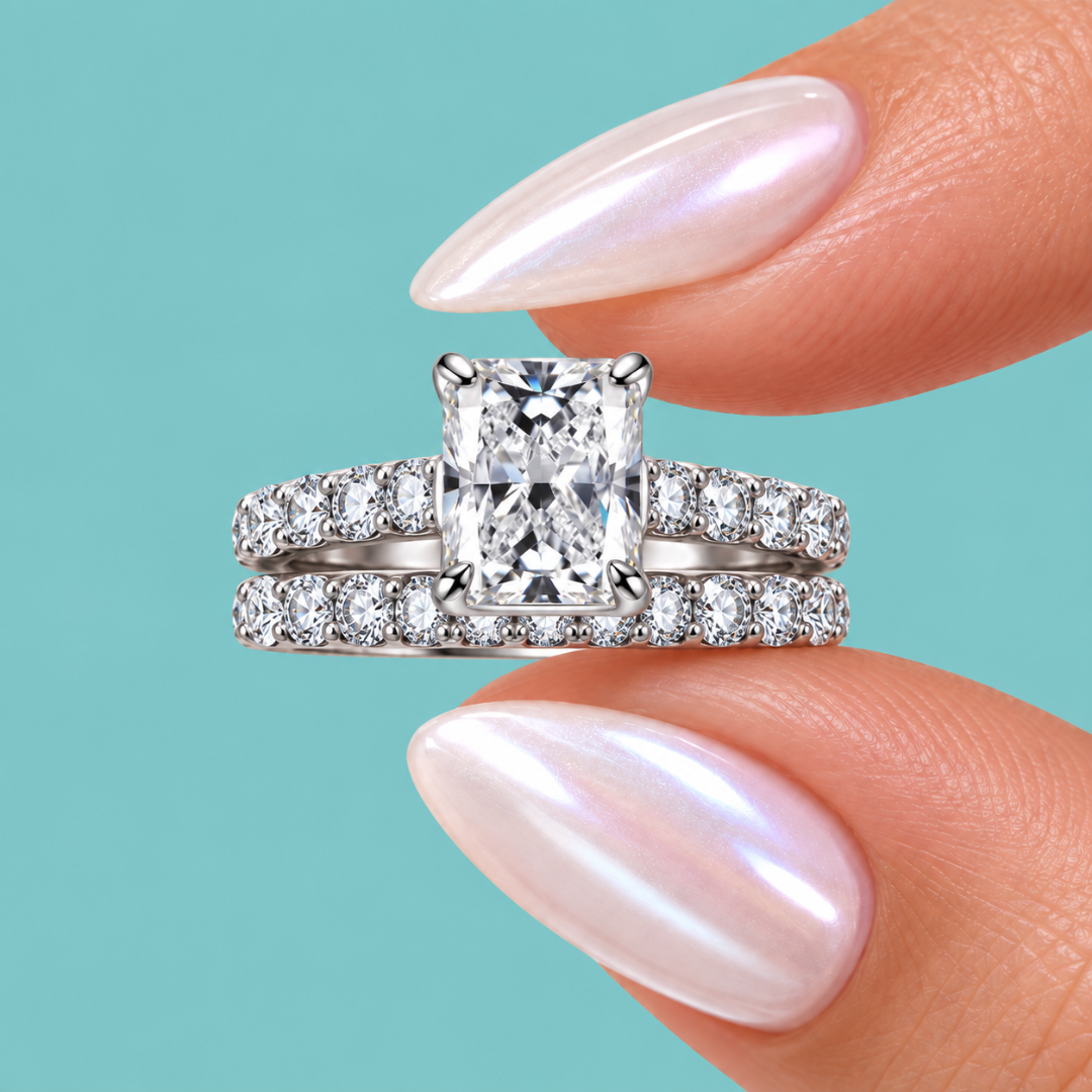 A radiant cut diamond engagement ring with a matching pavé band, held between fingers with iridescent nail polish against a solid turquoise background.