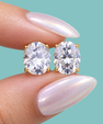 oval moissanite stud earring with a clear gemstone in a gold setting, against a solid teal background.
