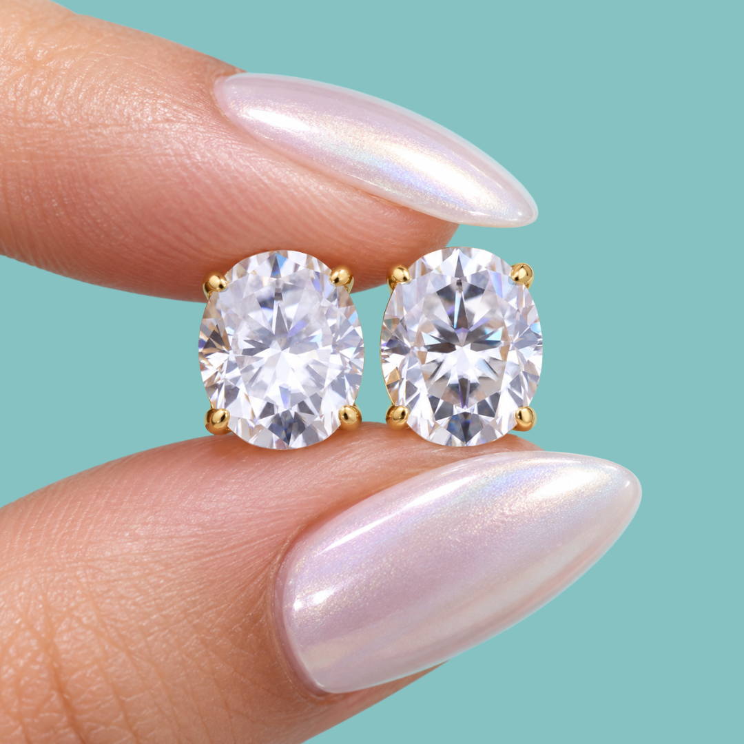 oval moissanite stud earring with a clear gemstone in a gold setting, against a solid teal background.