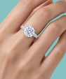A close-up of a hand wearing a radiant knife edge engagement ring with a silver-toned band, set against a solid light teal background.