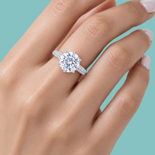 A close-up of a hand wearing a radiant knife edge engagement ring with a silver-toned band, set against a solid light teal background.