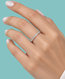 A close-up of a hand wearing a thin silver eternity ring set with small clear stones, against a solid light teal background.