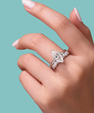 A close-up of a hand wearing a silver-toned ring with a marquise-cut center stone and smaller side stones, set against a solid turquoise background.