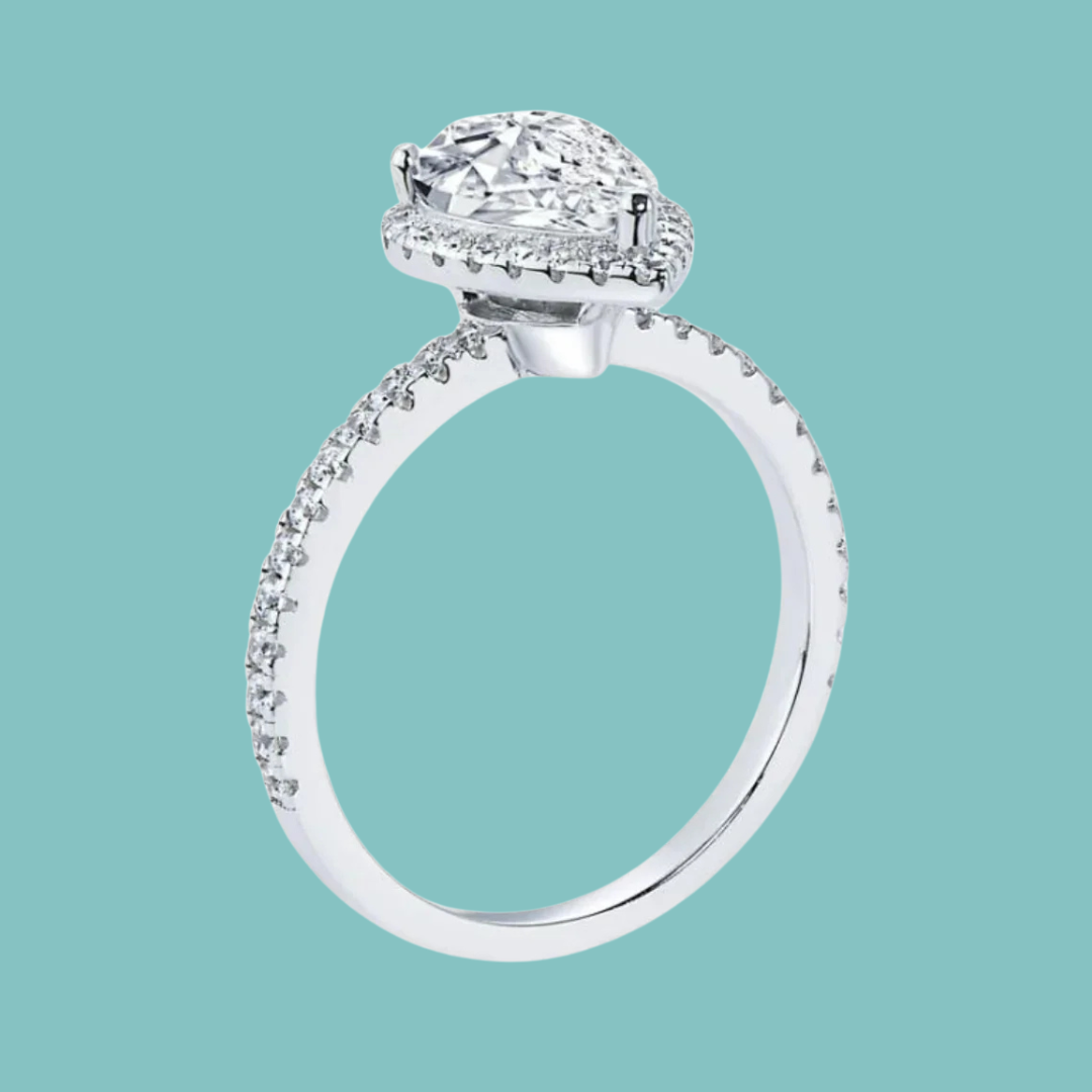 A silver-toned halo ring with a large oval center stone and small pavé accents along the band, shown on a solid light teal background.