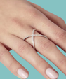 Modern crossed band moissanite ring held between fingers