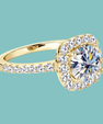 A yellow gold halo ring featuring a large round brilliant-cut center stone surrounded by a double halo of smaller stones, with the band accented by pavé-set round stones, shown on a solid teal background.