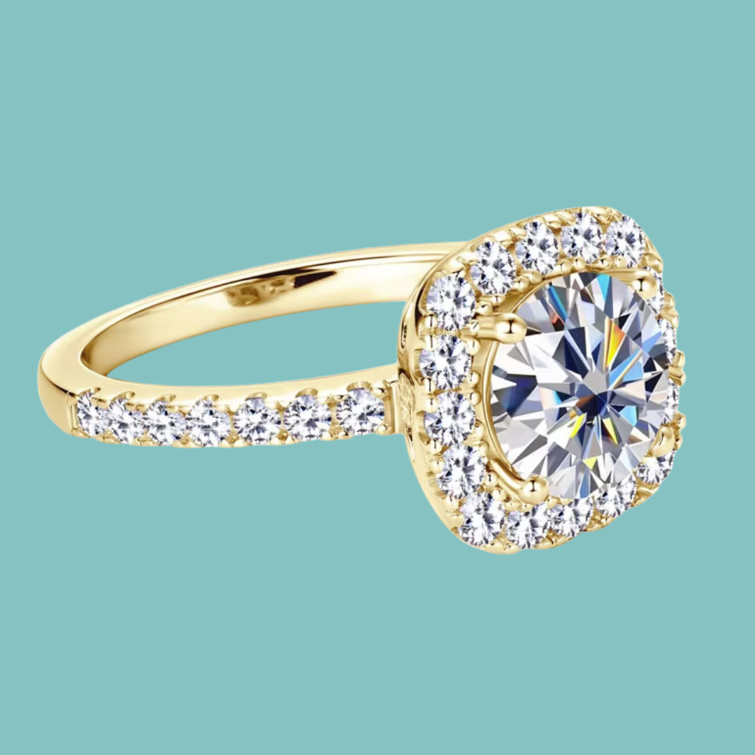 A yellow gold halo ring featuring a large round brilliant-cut center stone surrounded by a double halo of smaller stones, with the band accented by pavé-set round stones, shown on a solid teal background.