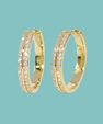 A pair of gold hoop earrings with pavé-set clear stones on the front, shown against a solid light teal background.