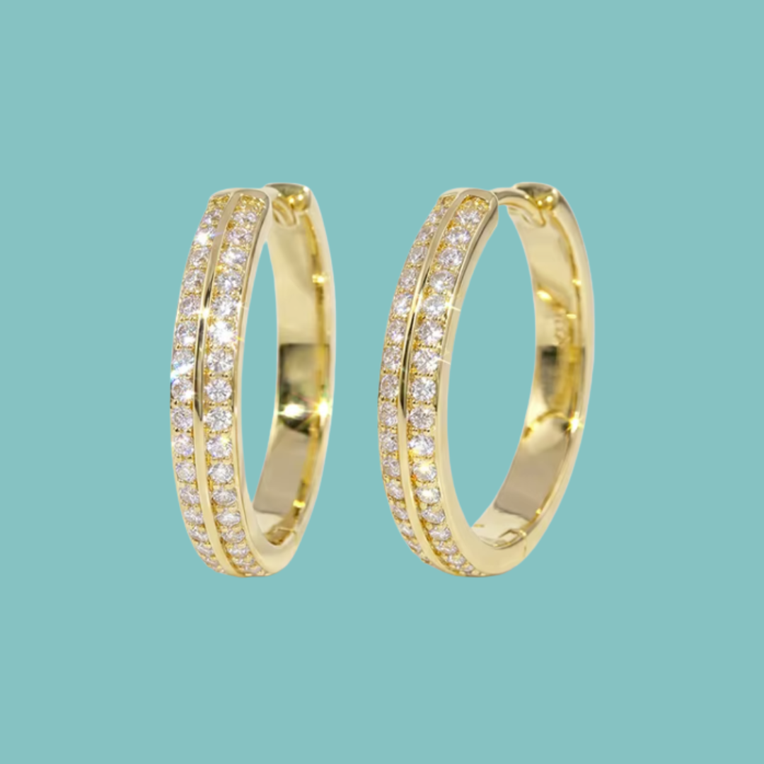 A pair of gold hoop earrings with pavé-set clear stones on the front, shown against a solid light teal background.