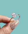 Silver ring with a large diamond held by a hand against a teal background