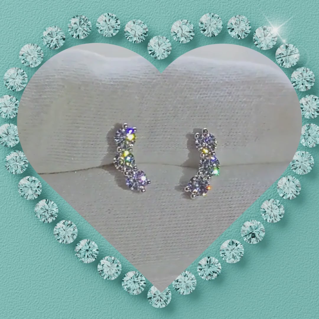 Close up of three stone moissanite earrings in a silver claw setting